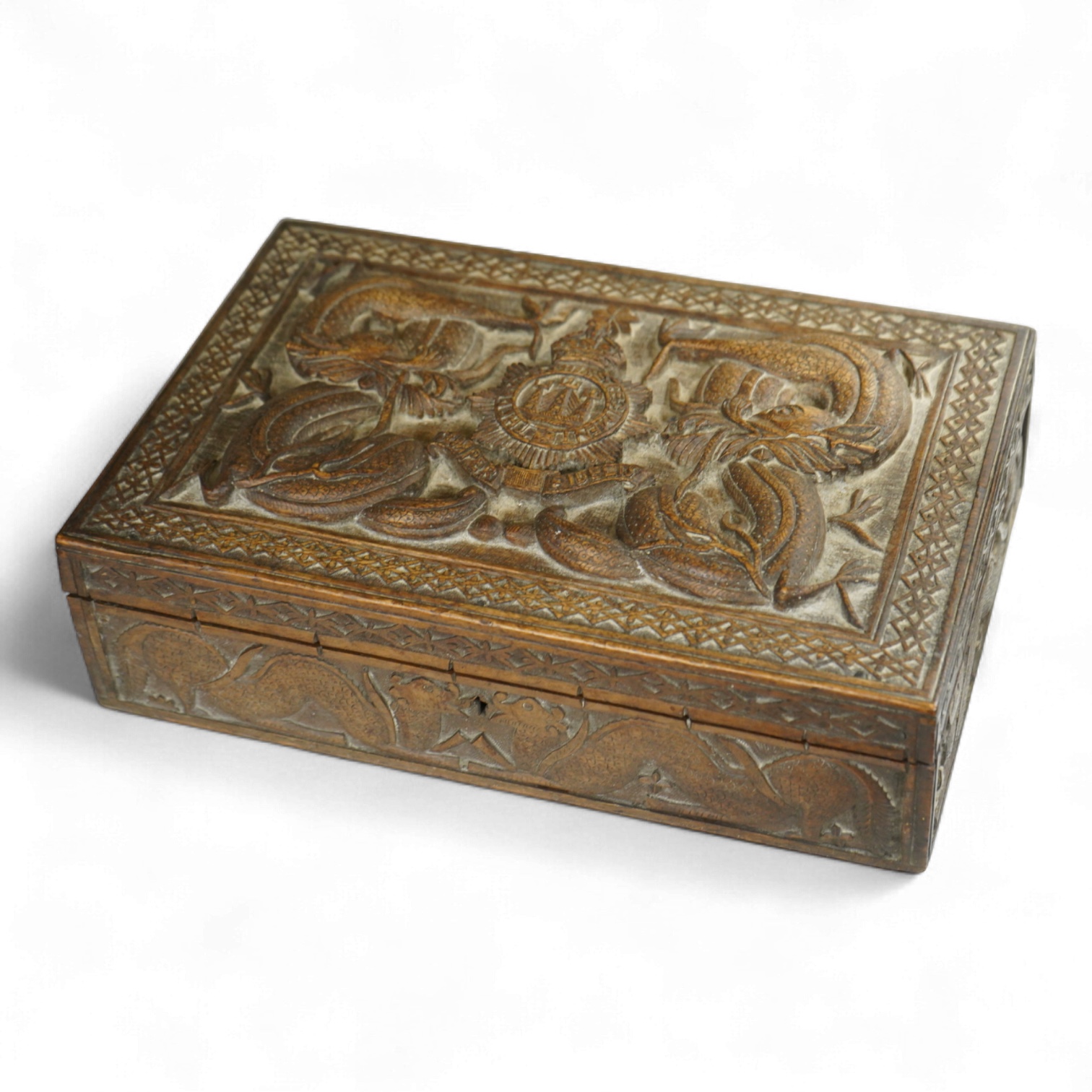 A Burmese military themed carved box, early 20th century, heavily carved with the insignia of the Devonshire Regiment to the lid, surrounded by mythical dolphins, serpents, and geometric patterns, with segmented interior